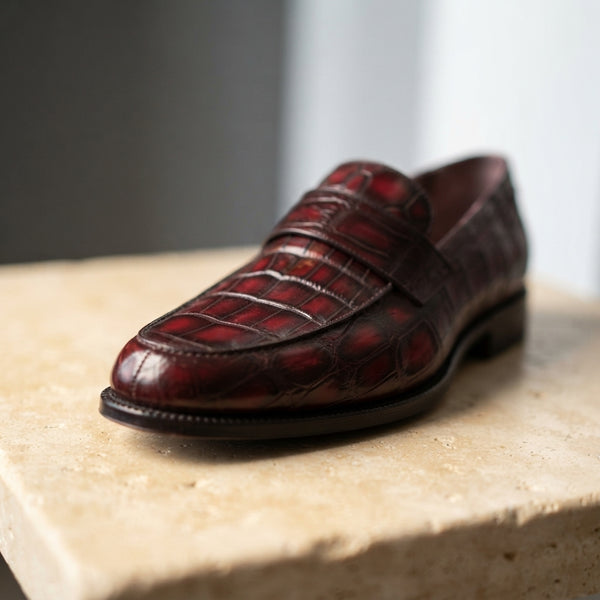 Close-up of red crocodile leather loafer showing detailed scales and a rich, aged patina on a stone surface.